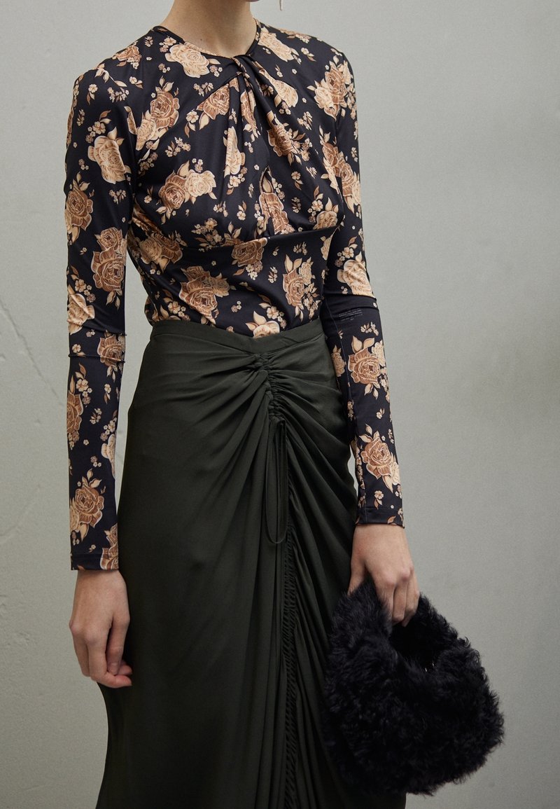 Blusa nera a manica lunga con fiori e rose pesche, abbinata a una gonna di seta verde scuro con drappeggio e una borsa nera morbida.