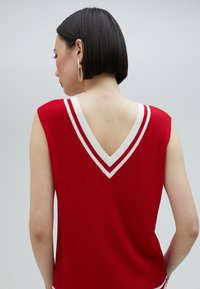 Röd ribbad ärmlös topp med vit V-halsringning, som har röda och vita ränder på baksidan, vilket skapar en sportig design.