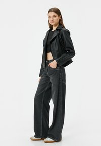 Zwarte leren cropped jas met brede grijze spijkerbroek. De outfit bevat een fitted zwart top en lichtgekleurde sneakers. Minimalistisch ontwerp.