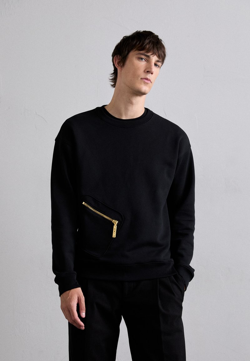 Čierna mikina so jedinečným šikmým zipsovým vreckom so zlatým kovom. Obsahuje klasický výstrih a voľný strih, vyrobená z hladkej látky.