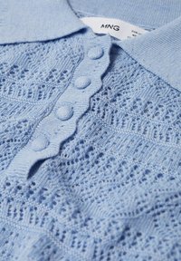 Haut tricot bleu clair avec un col festonné, présentant une patte de boutonnage avec des boutons ronds et un motif en dentelle texturé sur l'ensemble.