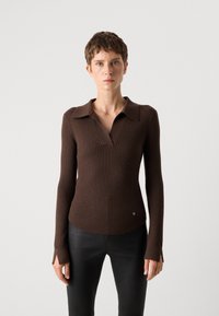 Rjav rebrast pleten bluza z dolgimi rokavi in polo ovratnikom, ki ima rahlo sijaj in majhne okraske. Prilegajoč dizajn poudari obliko.