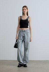 Juodas trumpintas tankinis su baltu krašteliu, šviesiai mėlynos platėjantys džinsai, juoda rankinė ir juodi platforminiai batai. Lygus audinys, kasdienis stilius.