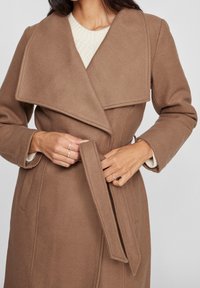 Brun ullblandad kappa med bred krage och bälte i midjan. Texturerad tyg med sidofickor och en mjuk innerfoder.