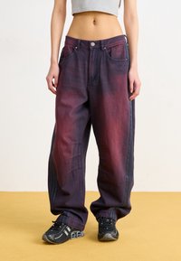 Baggy, gradientjeans i djup lila till röd nyanser, med hög midja, stora fickor och sidosträck. Matchas med svarta sneakers.