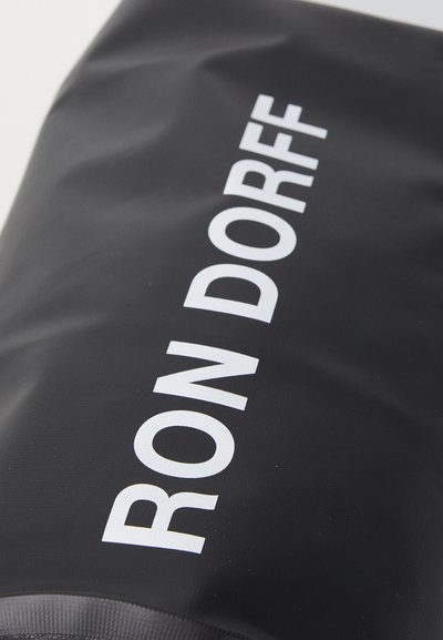 Mustmust kangas, millel on sile tekstuur ja suur valge tekst "RON DORFF" esiküljel selgelt välja toodud.