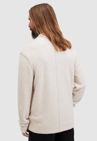 Cardigan color beige chiaro realizzato in materiale morbido, con vestibilità comoda, polsini a costine e una cucitura centrale sul retro.