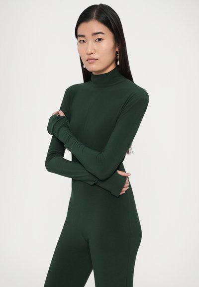 Body verde de manga larga con cuello alto, textura suave y diseño ajustado. Las mangas se extienden más allá de las muñecas para mayor cobertura.