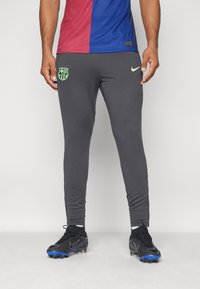Grijze sportbroek met een aansluitende pasvorm, voorzien van een groen logo op de dij en gecombineerd met zwarte voetbalschoenen. Glad uiterlijk, minimalistisch ontwerp.