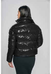 Svart dunjacka med glansig yta, med horisontellt quiltade sektioner och hög krage, bärs över en figursydd mörk kjol.