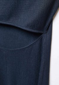 Tissu côtelé bleu foncé avec un gros plan sur des coutures en couches et des coutures qui se chevauchent dans un matériau doux texturé.