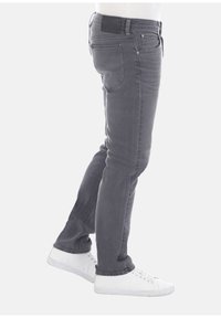 Vaqueros gris ajustados hechos de denim. Presentan cinco bolsillos, pasadores de cinturón y una etiqueta de cuero negro en la parte posterior. Combinados con zapatillas blancas.