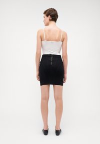 Fustă din denim negru cu un design ajustat, având un fermoar la spate și detalii de cusătură. Asortată cu un tricou fără mâneci alb și pantofi negri.