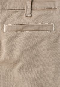 Beige fabric with a horizontal welt pocket and visible stitching, showing part of a belt loop above the pocket.