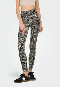 Leggings negro y crema con patrones geométricos que presentan círculos y triángulos; diseño de cintura alta; material elástico.