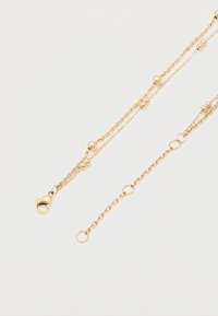 Λεπτό κολιέ με διπλή χρυσή αλυσίδα και μικρές στρογγυλές χάντρες, με κούμπωμα σε σχήμα αστακού, σε λευκό φόντο.