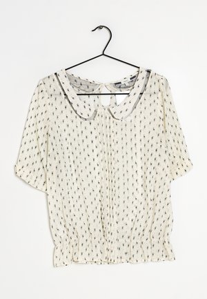 Witte blouse met klein zwart patroon, Peter Pan-kraag, halflange mouwen, sleutelgat aan de achterkant en gevormde zoom, hangend aan een zwarte hanger tegen een witte achtergrond.