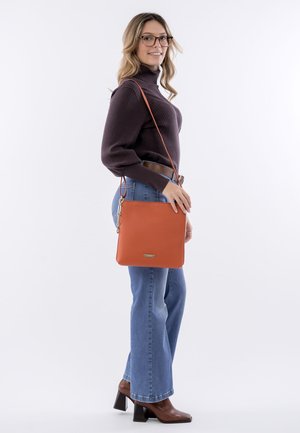 Orange leather handbag with a smooth texture, square shape, and discreet logo. Features a long strap for crossbody wear.
