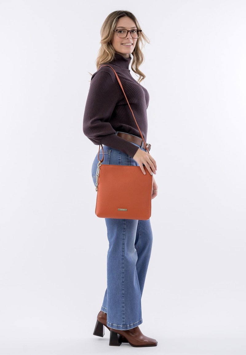 Orange leather handbag with a smooth texture, square shape, and discreet logo. Features a long strap for crossbody wear.