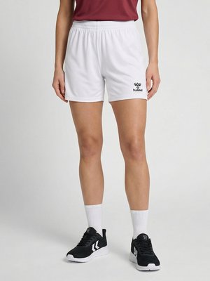 Person iført hvide Hummel sportsshorts, sorte og hvide sneakers og hvide sokker, står mod en ensfarvet baggrund.