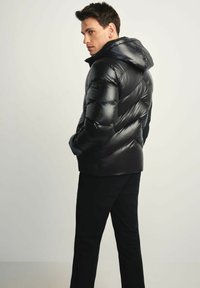 Czarna kurtka puchowa z kapturem charakteryzuje się pikowanym wzorem, błyszczącym wykończeniem i elastycznymi mankietami, w połączeniu z czarnymi spodniami, tworząc elegancki wygląd.