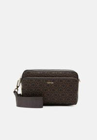 Ciemnobrązowa torba na ramię Calvin Klein z powtarzającym się wzorem logo CK, przednią kieszenią na zamek oraz regulowanym materiałowym paskiem z tłoczonym logo.