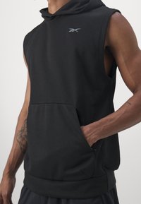 Svart ärmlös hoodie i mjukt tyg, med en känguruficka och en liten logga på bröstet. Slät textur och avslappnad passform.