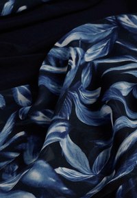Tessuto floreale con sfondo blu navy, caratterizzato da foglie blu e bianche che si avvolgono. Texture morbida con intricati motivi di foglie in tutto il tessuto.