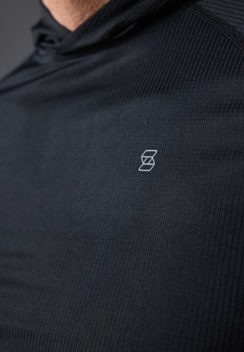 Czarna bluza z kapturem uszyta z teksturowanej tkaniny, z subtelnym logo na klatce piersiowej. Projekt zawiera ryflowane detale i dopasowany krój.