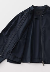 Marineblauwe bomberjack met een gladde textuur, voorzien van een volledige rits, drukknoopsluitingen en een zijzak. Binnenvoering van een vergelijkbare stof.