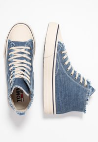 Vysoké tenisky v modrém denimovém provedení, s roztrhanými okraji, béžovou špičkou a tkaničkami. Mají texturovanou podrážku a decentní pruhový akcent.