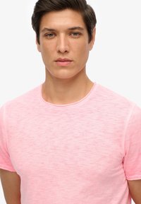 Camiseta de cuello redondo rosa con una tela suave y texturizada. Manga corta y diseño minimalista, con un ligero patrón jaspeado.