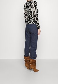 Černý a krémový vzorovaný dlouhý rukáv, modré džínové kalhoty a hnědé semišové boty na podpatku; viditelné švy a volný střih bot.