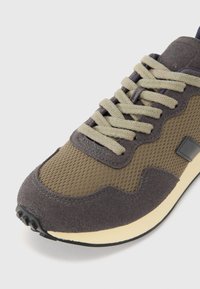 Sneakers con una combinazione di mesh verde oliva e suede grigio scuro. Presentano una punta arrotondata, suola beige e lacci verdi a contrasto.