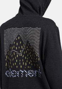 Felpa con cappuccio nera, caratterizzata da una grafica di montagne verdi con linee ondulate sopra e testo decorato nella parte inferiore, realizzata in tessuto morbido.