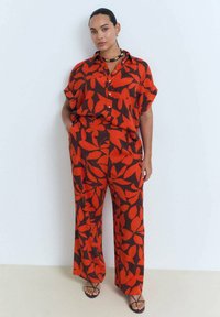 Red and black patterned two-piece outfit featuring a short sleeve button-up shirt and loose-fitting pants, made of lightweight fabric.
