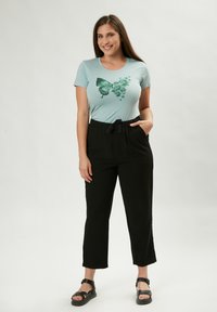 T-shirt azzurro chiaro con una grafica di una farfalla verde, abbinato a pantaloni neri a vita alta, larghi, con tasche e cordino.