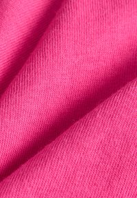 Tissu rose vif avec une texture lisse et douce et un motif fin côtelé, drapé en plis se chevauchant, mettant en valeur son matériau léger.