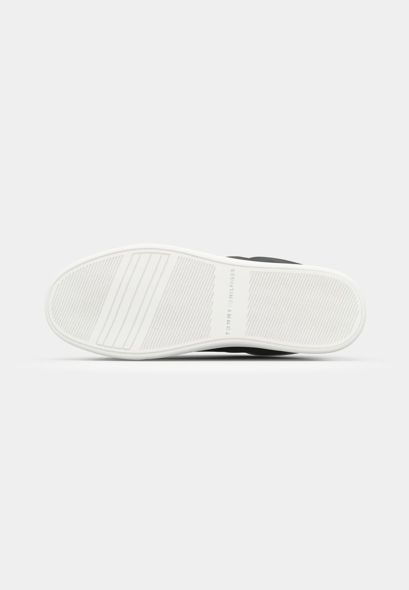 Suola nera di sneaker con righe orizzontali, caratterizzata da una suola in gomma bianca e un marchio stampato di lato. Superficie liscia, dettagli minimi.