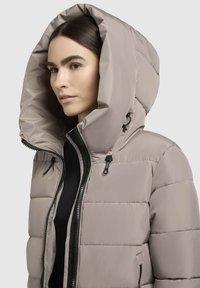 Puffer jacket in light gray with a large hood, featuring a zip closure and adjustable drawstrings. The fabric is smooth and slightly glossy.