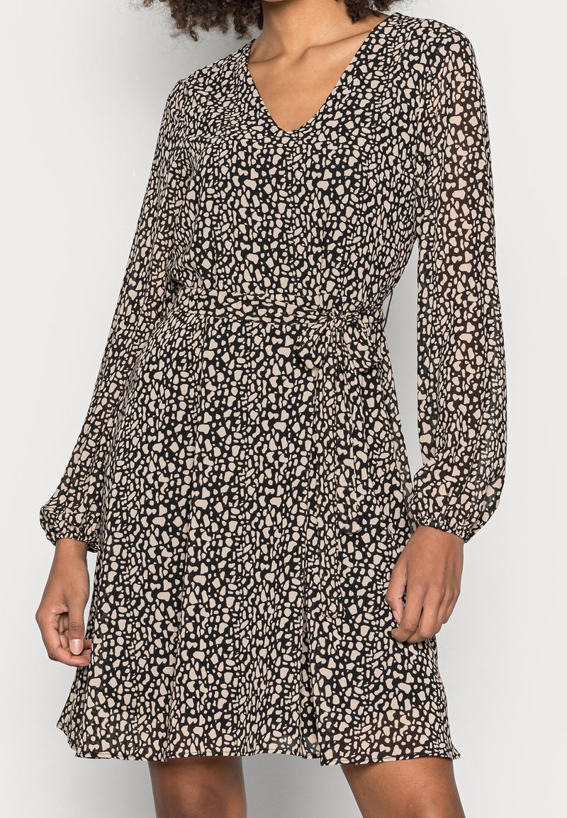 Robe à motifs noirs et beiges avec manches longues, décolleté en V et taille cintrée, en tissu fluide et léger.