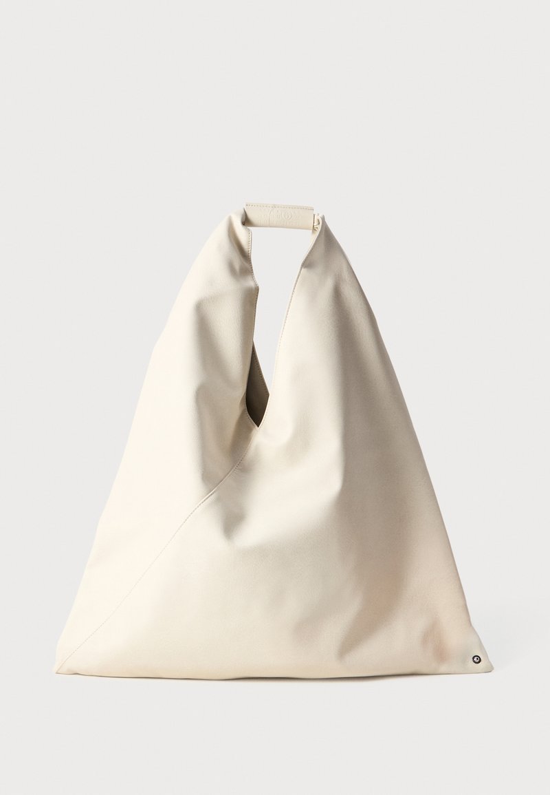 Beige, mjukt texturerad väska med ett unikt vridet handtag och diagonala sömn detaljer. Minimalistisk design med en rund accent i botten.