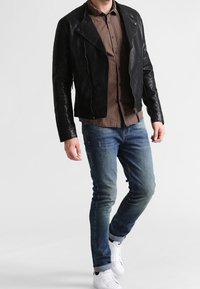 Chaqueta de motociclista de cuero negro con cierre frontal de cremallera, camisa a cuadros de contraste, vaqueros azules y zapatillas blancas.