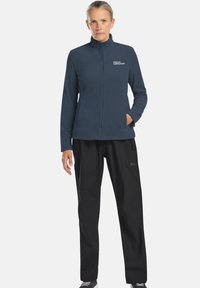 Fleecejacke in Dunkelblau mit hohem Kragen und Reißverschluss, kombiniert mit schwarzen Hosen. Beide Kleidungsstücke zeichnen sich durch ein modernes, funktionales Design aus.