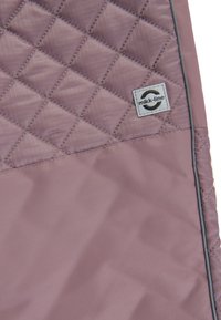 Gepolsterte Außenlage in sanftem Mauve mit kontrastierendem grauen Rand, versehen mit einem Logo-Tag. Glatte Textur und Rautenmuster-Detail.