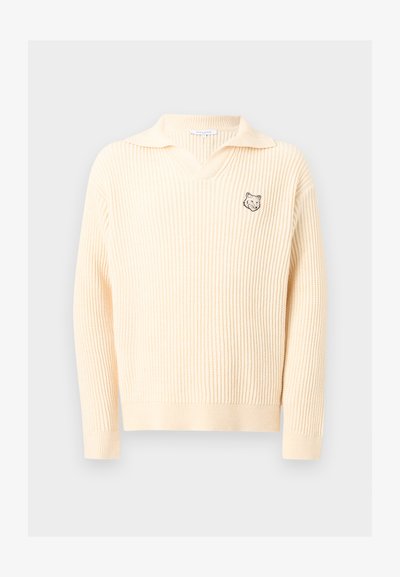 Pull en maille côtelée couleur crème avec un col et un petit logo de tête de loup sur le côté gauche de la poitrine.