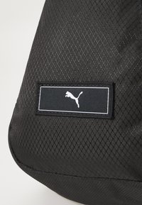 Geantă texturată neagră, fabricată dintr-un material durabil, având un model în diamant. Pachet cu logo cu contur alb și silueta puma.