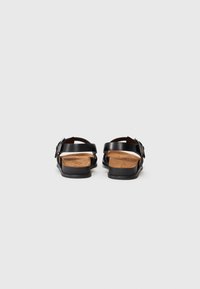 Zwarte leren sandalen met een houten binnenzool, open achterkant, verstelbare band met zilveren gesp en gestructureerde rubberen zool.