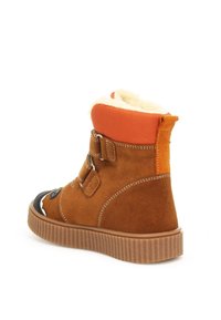 Bruine suède enkellaars met oranje stoffen trim, schapenvachtvoering, twee gespen en een zwarte rubberen neuskap. Gegolfde rubberen zool met textuur.