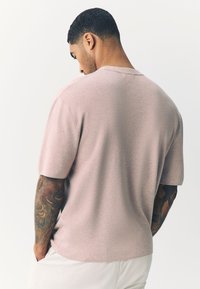 Ljusrosa kortärmad skjorta med rund halsringning, sömlös axeldesign och texturerad yta, tillsammans med ljusfärgade byxor.